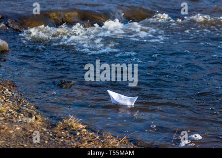 Ein Papier Boot auf eine turbulente Strom von Wasser kämpft mit der Strömung. Kleines Papier Boot fließt entlang des Flusses Stockfoto