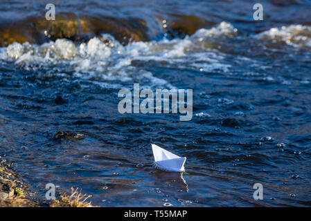 Ein Papier Boot auf eine turbulente Strom von Wasser kämpft mit der Strömung. Kleines Papier Boot fließt entlang des Flusses Stockfoto