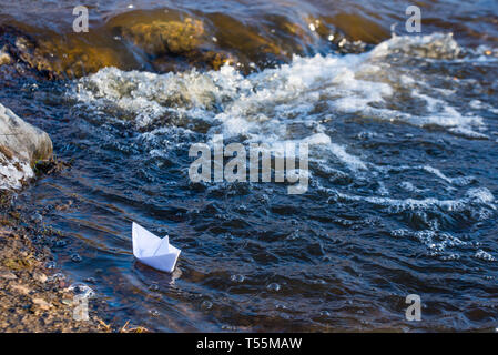 Ein Papier Boot auf eine turbulente Strom von Wasser kämpft mit der Strömung. Kleines Papier Boot fließt entlang des Flusses Stockfoto