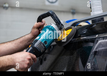 Nahaufnahme auf die Hände eines Mannes, der Arbeiter, der hält ein Werkzeug Polierer zum Polieren das Dach eines Autos während der Arbeit in einem Fahrzeug mit Werkstatt. Au Stockfoto