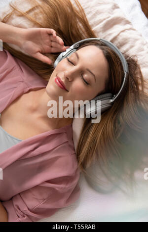 Junge Frau, hören Sie Musik auf Bett Stockfoto