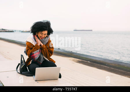 Junge Frau mit Laptop auf der Uferpromenade in Lissabon, Portugal. Stockfoto