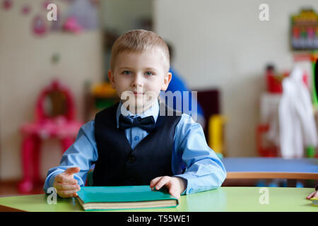 Eine Vorschule Junge an einem Tisch sitzt mit einem Buch Stockfoto