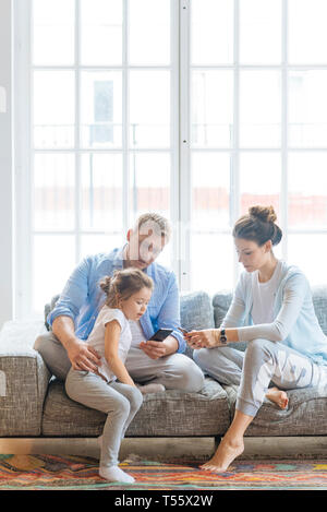 Eltern halten Smartphones auf Sofa mit Ihrer Tochter Stockfoto