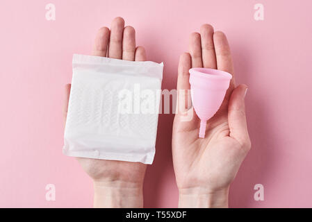 Frau Hände halten Sanitär pad und menstruationsschale auf rosa Hintergrund Stockfoto