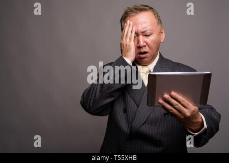 Portrait von Reifen asiatische Geschäftsmann gegen grauer Hintergrund Stockfoto