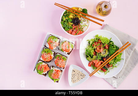 Gesundes Frühstück. Buddha Schüssel mit Reis, Mango, Avocado und Lachs und frischer Salat mit Tomaten, Avocado, Rucola, Samen, Lachs und Lachs Sandwich Stockfoto