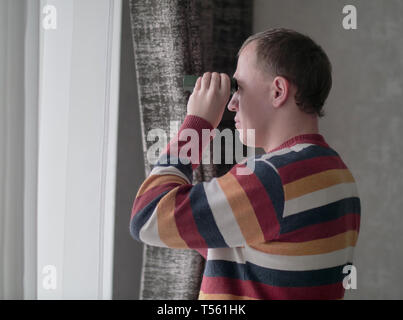 Man schaut aus dem Fenster durch ein Fernglas Stockfoto