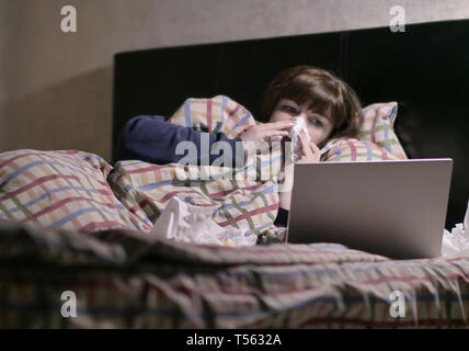 Sick hübsches Mädchen liegt abends im Bett und beobachtete einen Laptop Stockfoto