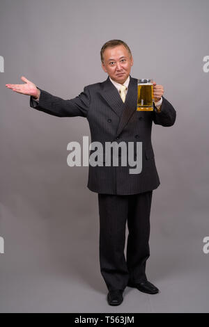 Portrait von Reifen asiatische Geschäftsmann gegen grauer Hintergrund Stockfoto