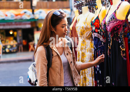 Junge weibliche Asiatische tourist Frau Shopping und der Auswahl der Kleider auf Street Market in Bangkok, Thailand