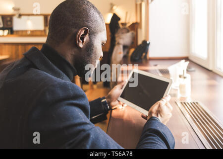 Junge hübsche dunkelhäutige Geschäftsmann mit Tablette im Cafe. Stockfoto