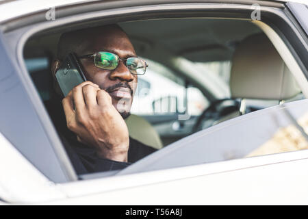 Junge erfolgreiche Geschäftsmann am Telefon zu sprechen auf dem Rücksitz eines teuren Auto sitzen. Verhandlungen und Meetings. Stockfoto