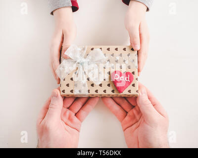 Die Hände des Kindes und die Hände des erwachsenen Mannes, schönen Geschenkkarton, Farbband und glasierte Plätzchen auf einem weißen, Holz- Hintergrund. Ansicht von oben, close-up. Vorbereitung für Th Stockfoto