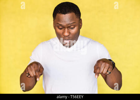 African American man schaut, bringt surprisement angeben, mit Zeigefinger am Boden. Stockfoto
