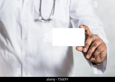 Hübscher junger Arzt in einem weißen Mantel mit einem Stethoskop hält auf der ausgestreckten Hand einen leeren weißen Karton für die Blister Paket von Pillen. Mock up. Stockfoto