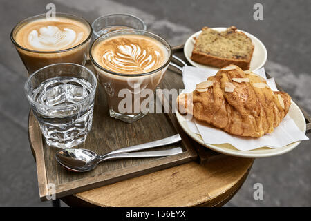 Milch Kaffee mit Croissant, Brot und Wasser auf hölzernen Tisch Stockfoto