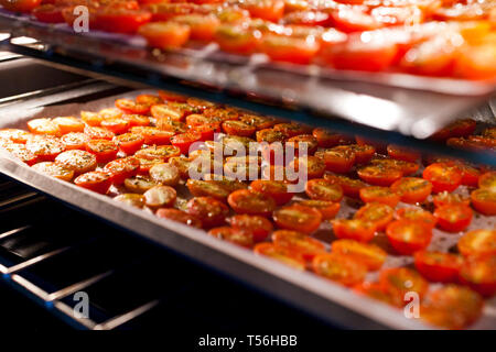 Schalen mit frischen Kirschtomaten auf Gestellen trocknen im Ofen Stockfoto