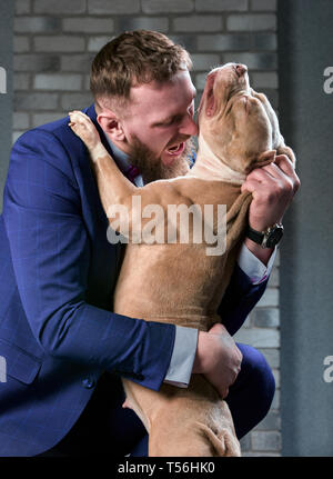 Hund Bulli und ihre Besitzer, ihre liebevolle Meister, der den Hund in ihren Armen, Umarmungen und Küsse hält. Der Hund fühlt sich gut auf die Hand des Besitzers Stockfoto