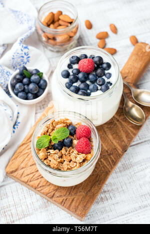 Joghurt mit Müsli, Heidelbeere, Himbeere im Glas. Gesundes Frühstück essen, weiß Holz- Hintergrund Stockfoto