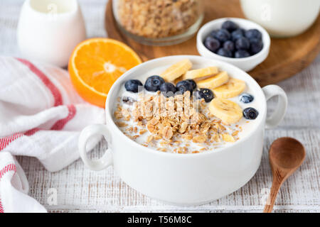 Frühstück Müsli Schale mit Banane und Heidelbeeren auf weissem Holztisch. Detailansicht. Konzept der gesunden Frühstück, gesunde Ernährung Stockfoto