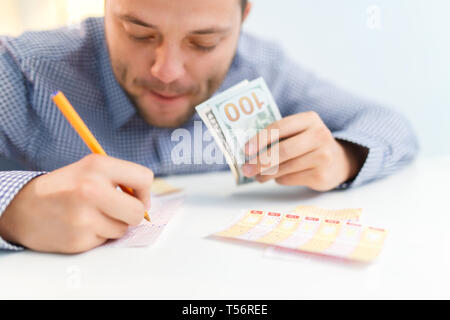 Foto der männlichen Ausfüllen Lottery ticket und Euro, beim Sitzen am Tisch Stockfoto