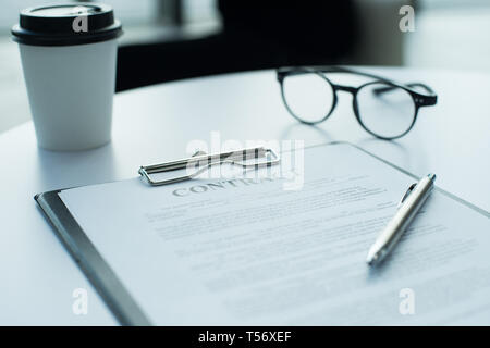 Eine Brille, Stift, Kaffee und Vertrag liegen oben auf Tabelle Stockfoto