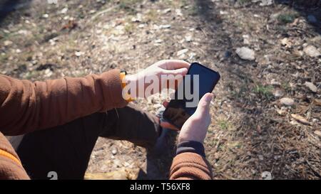 Thema Tourismus und Technologie. Jungen kaukasischen Mann Wandern touristische in einem Pinienwald verwendet die Technologie, Hand, Mobiltelefon, um den Bildschirm zu berühren. Gps Stockfoto