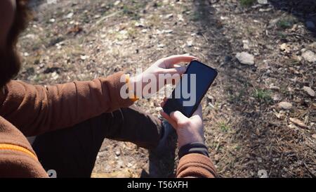 Thema Tourismus und Technologie. Jungen kaukasischen Mann Wandern touristische in einem Pinienwald verwendet die Technologie, Hand, Mobiltelefon, um den Bildschirm zu berühren. Gps Stockfoto