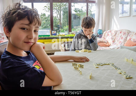 Ein Junge posiert für ein Foto, während Sie ein Spiel spielen der Domino mit seinem Bruder auf einen Esstisch. Stockfoto