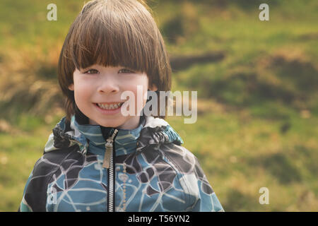 Kleine lächelnde junge Portrait auf grünem Gras Hintergrund, matt Stockfoto