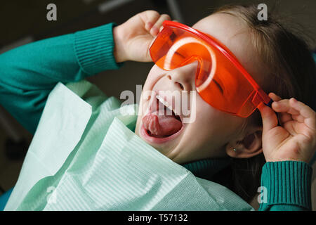 Kleines Mädchen sitzt in der zahnmedizinischen Stuhl und trägt eine Schutzbrille. Sie Plantscht. Stockfoto