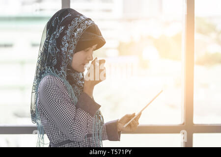 Islam muslimische Frau trinkt Kaffee, während bei Tablet suchen Stockfoto