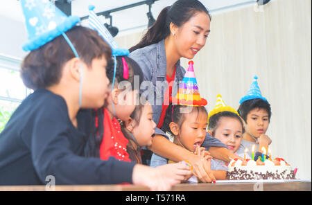 Gruppe von Kindern weht Geburtstagstorte in Geburtstag Happy Birthday gesungen Stockfoto