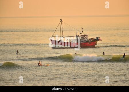 Aberystwyth, Wales, UK. 21. Apr 2019. Ein Fischerboot kehrt zum Hafen vorbei an Surfer auf eine wunderbar warmen und sonnigen Ostersonntag Abend in Aberystwyth Wales als Land genießt die herrlich warmen Feiertag Wetter. Die Temperatur erreicht 23 Grad Celsius bei Trawsgoed nur im Inland von der Twin und ist damit der heißeste Platz in Wales heute Credit: Keith Morris/Alamy leben Nachrichten Stockfoto