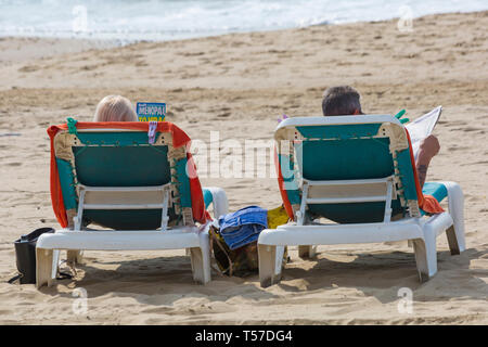 Bournemouth, Dorset, Großbritannien. 22 Apr, 2019. UK Wetter: Nach einem dunstigen Start das herrliche Wetter mit warmen und sonnigen Wetter fort, als beachgoers Kopf zum Meer die Wärme und Sonnenschein in Bournemouth Strände am Ostermontag zu genießen, bevor das Wetter ändert sich und die Rückkehr zur Arbeit. Paar Sonnenbad auf den Liegestühlen zu lesen. Credit: Carolyn Jenkins/Alamy leben Nachrichten Stockfoto