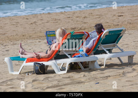 Bournemouth, Dorset, Großbritannien. 22 Apr, 2019. UK Wetter: Nach einem dunstigen Start das herrliche Wetter mit warmen und sonnigen Wetter fort, als beachgoers Kopf zum Meer die Wärme und Sonnenschein in Bournemouth Strände am Ostermontag zu genießen, bevor das Wetter ändert sich und die Rückkehr zur Arbeit. Paar Sonnenbad auf den Liegestühlen zu lesen. Credit: Carolyn Jenkins/Alamy leben Nachrichten Stockfoto