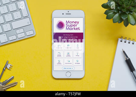 Ein iPhone mit dem Geld Supermarkt website ruht auf einem gelben Hintergrund Tabelle mit einer Tastatur, Tasten, Notepad und Anlage (nur redaktionelle Nutzung). Stockfoto