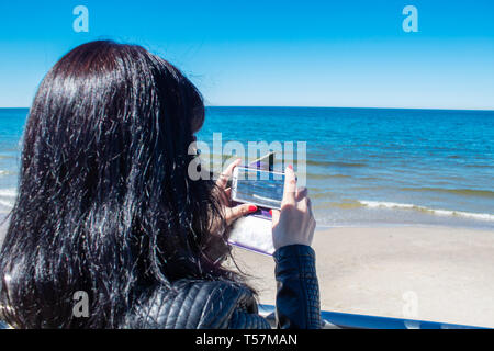 Junge Frau mit einem mobilen Smartphone Foto auf das Meer auf der sonnigen Tag zu nehmen Stockfoto