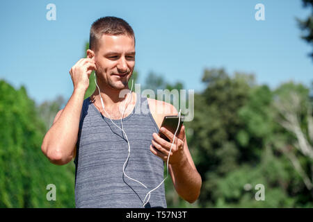 Junger Mann mit Ohrhörer Üben Yoga im Freien im Park holding Smartphone Musik lächelt Fröhlich Stockfoto
