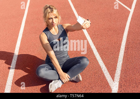 Junge Frau Athlet auf Stadion sportlicher Lifestyle sitzen auf Titel Taking selfie Foto auf dem Smartphone lächelnd freudige Draufsicht Stockfoto