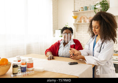 Junge Krankenschwester unter Berücksichtigung der Blutproben von Frau mit Diabetes Stockfoto