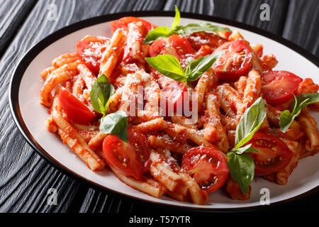 Casarecce Nudeln mit würziger Tomatensoße, Parmesan und Basilikum mit der Zugabe von frischen Tomaten auf einem Teller auf den Tisch. Horizontale Stockfoto