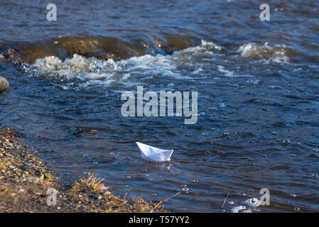 Ein Papier Boot auf eine turbulente Strom von Wasser kämpft mit der Strömung. Kleines Papier Boot fließt entlang des Flusses Stockfoto