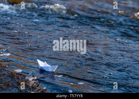 Ein Papier Boot auf eine turbulente Strom von Wasser kämpft mit der Strömung. Kleines Papier Boot fließt entlang des Flusses Stockfoto