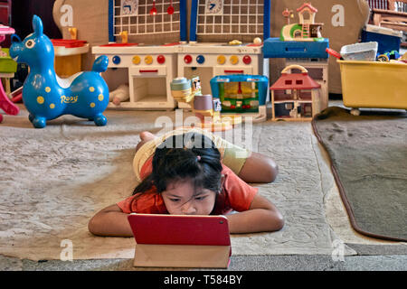 Kind mit iPad. Junge Mädchen mit ihrem modernen iPad und ignoriert ihre traditionellen Spielzeug. Konzept von alt vs neu. Stockfoto