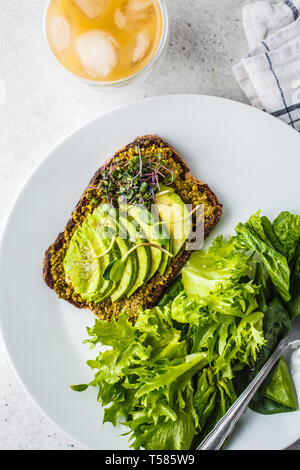 Avocado Toast mit Pesto, Sprossen und Salat auf einem weißen Teller und Eis Kaffee. Stockfoto