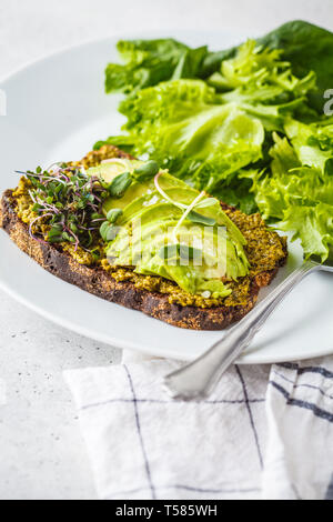 Avocado Toast mit Pesto, Sprossen und Salat auf einem weißen Teller. Stockfoto