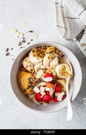 Müsli mit Beeren, Banane, Peanut Butter und Schokolade in einer weißen Schüssel. Gesund vegan Frühstück Konzept. Stockfoto