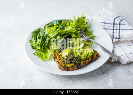 Avocado Toast mit Pesto, Sprossen und Salat auf einem weißen Teller. Stockfoto